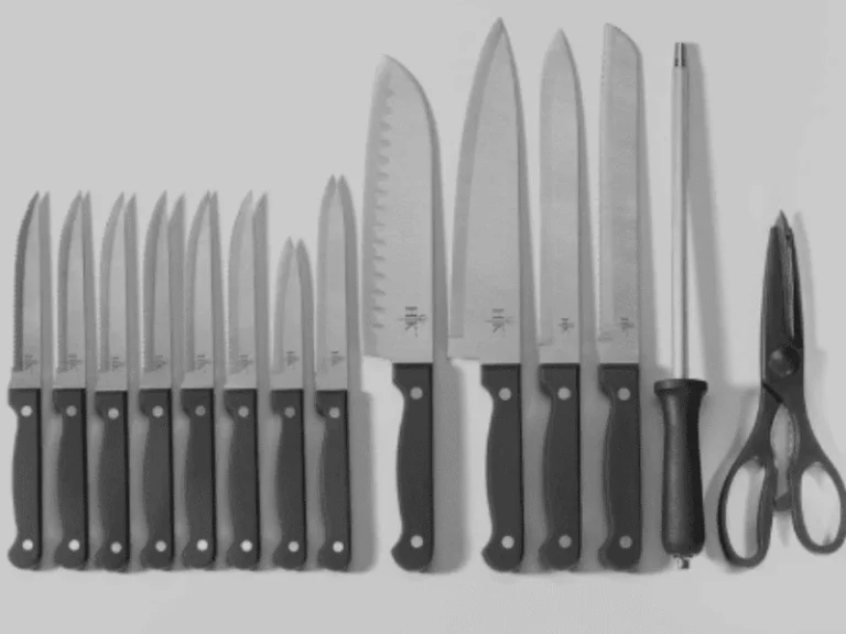 Full kitchen knife set including chef’s knives, steak knives, honing rod, and kitchen shears laid out on a flat surface.