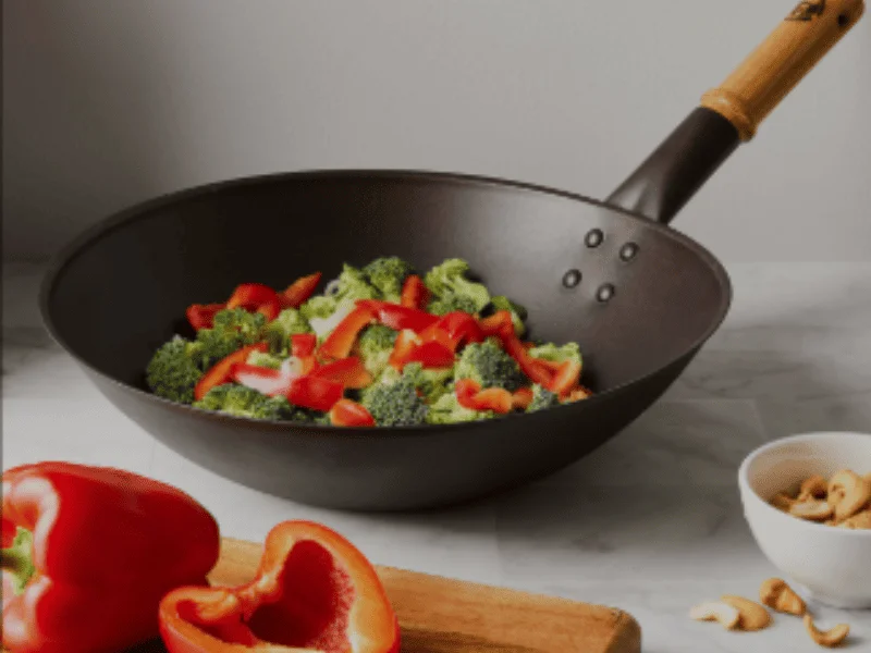 Fresh broccoli and red bell peppers in a wok pan with wooden handle, ready for stir-frying.