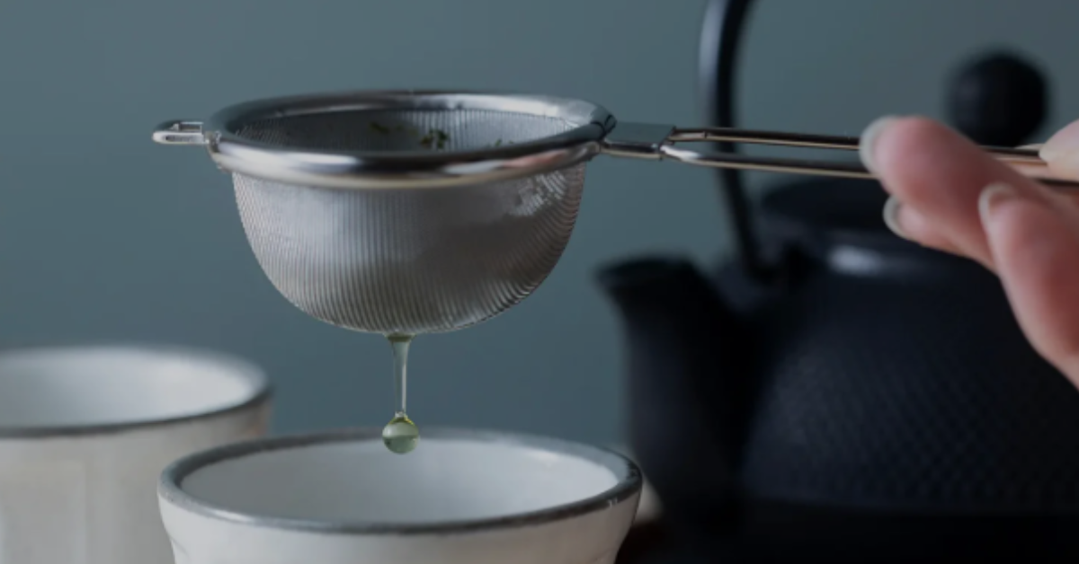 Tea infuser held above a cup with green tea dripping through it.