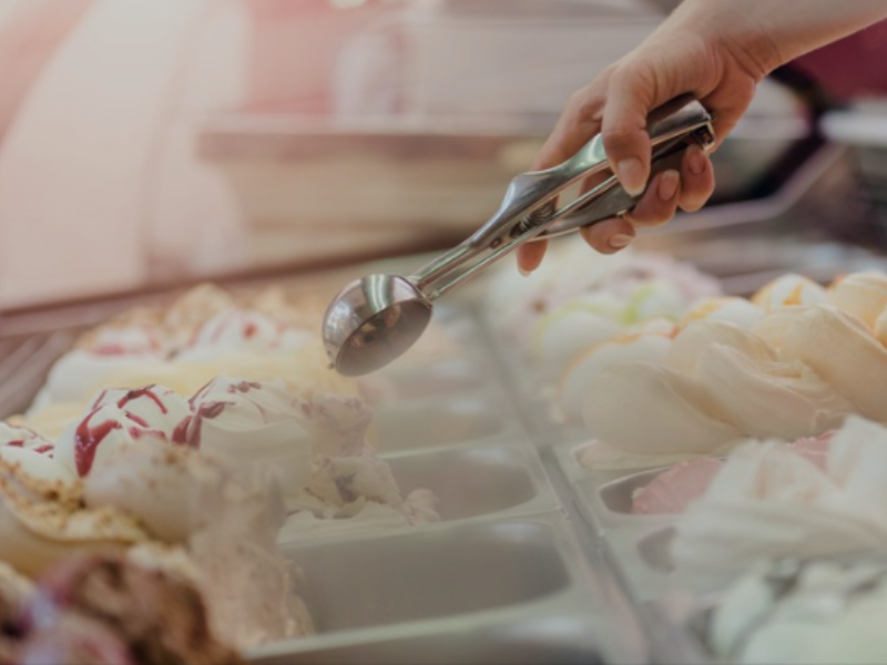 Ice cream scoop being used by hand to serve gelato from a display case in a dessert shop